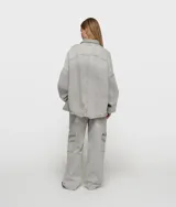 Camisa oversize de algodón orgánico con certificación GOTS, color gris claro con efecto lavado. Presenta cuello, cierre frontal de botones, dos bolsillos de parche en el pecho y puños elásticos.