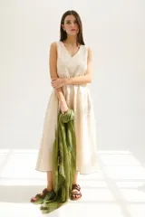 Vestido largo color beige claro, sin mangas, con escote en V y corte escalonado con frunces que le dan volumen.