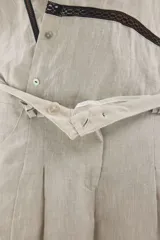 Pantalón de lino marrón de tiro medio, con calce holgado y diseño de piernas amplias. Cuenta con bolsillos traseros, trabillas para cinto y un pin bordado en contraste.