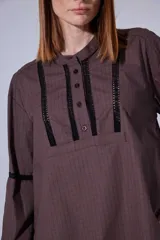 Camisa blanca de algodón con pechera decorada con alforzas y puntillas. Presenta cierre frontal con botones, mangas tres cuartos con frunces y detalles de puntilla, y un diseño de corte holgado con ruedo redondeado.