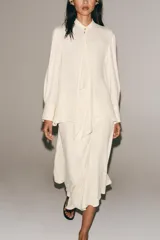Blusa de viscosa color marfil, con cuello mao, manga larga con puños anchos, cierre frontal con botones y detalle de lazada colgante en el frente.