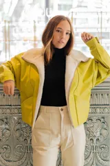 Chaqueta bomber de cuero color marrón, con cuello de piel sintética roja, cierre frontal con cremallera y bolsillos laterales.