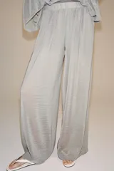 Pantalón palazzo gris de tejido semitransparente con tiro medio, cintura elástica, bolsillos laterales y forro interior corto.