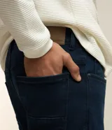Pantalón de jean corte slim, color azul oscuro, con trabillas en la cintura, cierre frontal y bolsillos laterales y traseros.