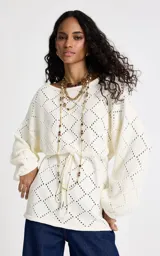 Sweater de punto color blanco con diseño geométrico calado. Presenta un amplio escote barco, mangas largas con volumen sutil y cintura ajustable mediante lazo frontal con terminaciones metálicas. Los puños y el bajo son acanalados.