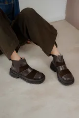 Botas de caña baja con punta cuadrada, confeccionadas en una combinación de cuero liso y gamuza en tonos marrones. Presentan un diseño con múltiples cortes y costuras visibles, cierre elástico lateral y suela de goma dentada tipo track.