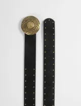 Cinturón negro de cuero vegano con textura tipo gamuza, decorado con pequeñas tachas doradas a lo largo de toda la tira. Presenta una hebilla circular grande de metal dorado con un diseño labrado y texturizado.