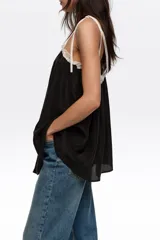 Top de diseño fluido en color negro con detalles de encaje blanco en el escote y tirantes finos regulables con lazos.