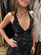 Vestido corto negro con estampado de plumas doradas, escote en V, breteles finos cruzados en la espalda, cut-outs laterales y volado en el ruedo.