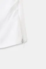 Top blanco de popelín con escote cuadrado y tiras cruzadas en la espalda. Presenta mangas globo abullonadas y detalle de frunces ajustables en los laterales inferiores.