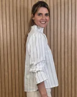 Blusa blanca de algodón con escote en V y cuello mao. Presenta mangas largas abullonadas con puños acampanados y fruncidos.