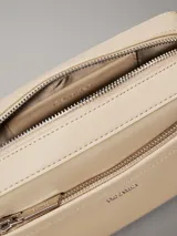 Cartera rectangular tipo bandolera de piel sintética color beige claro, con bolsillo exterior frontal y cierre superior de cremallera. Incluye dos correas desmontables: una ancha y una fina ajustable. Presenta el logo metálico de Calvin Klein en la parte frontal.