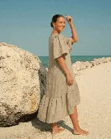 Vestido midi de lino color beige, con mangas cortas abullonadas, diseño fluido y volado en el ruedo asimétrico, más largo en la parte trasera.