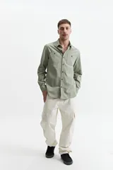 Camisa manga larga color verde oliva, corte slim fit, con cartera abotonada, dos bolsillos frontales con botón y confeccionada en 100% algodón.
