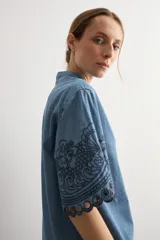 Camisa de denim celeste con cuello mao, botonadura frontal oculta y mangas cortas holgadas que presentan un delicado bordado floral oscuro y dobladillo calado.