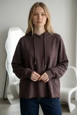 Buzo tipo canguro de corte oversize, color marrón oscuro, con capucha y cordones ajustables. Presenta costuras verticales decorativas, bolsillos laterales y ruedo con terminación desflecada.