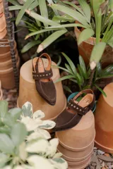 Zuecos de gamuza color marrón con taco cuadrado bajo y tira sobre el empeine decorada con tachas metálicas.