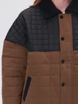 Campera acolchada con diseño de bloques de color en tonos terracota y beige. Presenta cuello camisero y puños en pana negra, cierre frontal oculto con botones a presión y costuras capitoneadas en toda la prenda.