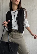 Chaleco negro de gamuza con detalles de tachas doradas a lo largo de la abertura frontal y los bordes.