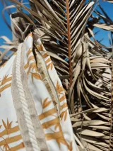 Sobre de tela color crudo con estampado de cañas color mostaza, detalles en yute y pulsera personalizada.