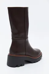 Bota de caña media en cuero sintético color negro, con diseño minimalista y suela robusta dentada con detalle de borde en color marrón.