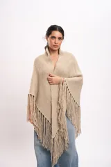 Poncho triangular tejido artesanalmente en telar manual, de lana merino color beige, con cuello alto y flecos largos en los bordes.