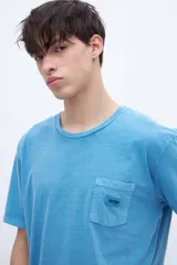 Remera celeste de algodón con bolsillo en el pecho, teñida en prenda. Tiene una etiqueta en el bolsillo y un estampado en la espalda.