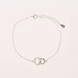 Pulsera de plata con dos anillos entrelazados como dije central, uno liso y otro con incrustaciones de circonias. Cuenta con cadena de eslabones finos, cierre de mosquetón y cadena de extensión con dije de "S925".