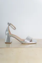 Sandalias plateadas de cuero vegano, con punta cuadrada, tira delgada sobre los dedos y pulsera al tobillo con hebilla. Taco cuadrado de 6 cm.
