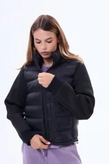 Campera negra de estilo híbrido, con cuerpo acolchado y mangas de tejido liso. Presenta cuello alto, cierre frontal y puños elásticos.