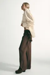 Pantalón de tiro medio con pernera recta y amplia, confeccionado en tejido con textura. Presenta una pieza superpuesta tipo pañuelo anudada en la cintura y bajo ajustable con botón.