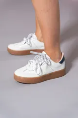 Championes de cuero blancos con suela de goma color caramelo y cordones moteados en blanco y negro.