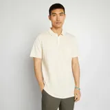 Remera tipo polo color crema, de piqué de algodón, con cuello clásico, tapeta de dos botones y bolsillo de parche en el pecho.
