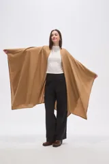 Poncho abierto de corte asimétrico y holgado, confeccionado en tejido de punto suave color beige, con mangas amplias y caída fluida.