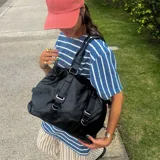 Bolso tipo tote negro de eco cuero con doble asa de hombro y cierre superior.