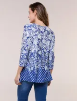 Blusa azul y blanca con estampado floral y geométrico, de calce suelto, con escote redondo, abertura tipo keyhole en el pecho, mangas tres cuartos y ruedo amplio con silueta evasé.