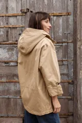 Parka liviana color beige con capucha, cierre frontal con botones, bolsillos delanteros con tapa y ajuste en la cintura. Presenta mangas con puños vueltos y detalle de botones.