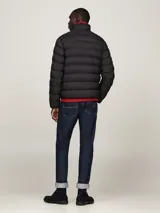 Campera acolchada negra de nailon con aislamiento térmico y acabado repelente al agua. Tiene cuello alto, cierre de cremallera, dos bolsillos delanteros y parche engomado del logo de Tommy Hilfiger en la manga.