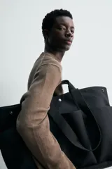 Bolso shopper negro fabricado en tejido técnico, con compartimento principal con cierre de botón a presión, múltiples bolsillos exteriores frontales, doble asa de mano y asas largas de hombro.