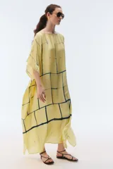 Kaftan maxi amplio de color amarillo, con escote redondo, mangas cortas y ruedo irregular. Presenta un diseño estampado a cuadros con efecto teñido.