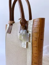Bolso matero de cuero color beige con textura de reptil y detalles en cuero marrón con textura de cocodrilo. Incluye manijas cortas de cuero marrón y dije de cruz plateada.