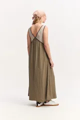 Vestido largo de silueta amplia y caída fluida, sin mangas, con escote en V y recorte bajo el busto. Combina un cuerpo superior beige con ribetes oscuros y una falda larga en color verde militar.