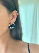 Aro de argolla pequeña en base de bronce dorado, decorado con cuentas de vidrio facetadas en colores azul y dorado. Tiene un diámetro de 2 cm y un diseño artesanal con alambre enrollado.