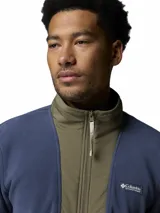 Campera de polar para hombre con cierre frontal completo. Presenta un diseño de bloques de color con cuerpo en azul y detalles en verde oliva en el cuello y la solapa central. Incluye bolsillos laterales con cierre y logo de la marca bordado en el pecho.
