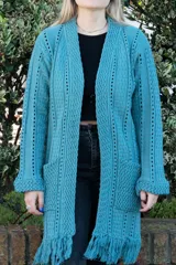 Sacón largo de tejido de punto calado color petróleo, con mangas largas y bolsillos delanteros. Presenta detalle de flecos en el ruedo.