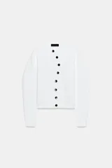 Chaqueta de punto de cuello redondo y manga larga, en color blanco, con cierre frontal asimétrico de botones negros.