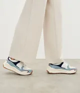 Championes estilo jogging con diseño de recortes contrastantes en tonos blanco, azul y gris. Presenta una parte superior de mesh respirable con sobreposiciones de poliuretano, forro suave y suela robusta de color crema con base marrón.
