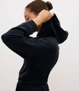 Campera deportiva de estilo utilitario color negro, confeccionada en tejido técnico. Presenta capucha, cierre frontal con botones, bolsillos con solapa en el pecho y lazo ajustable en la cintura. Posee mangas largas con puños y diseño liso.