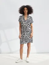 Vestido corto con estampado animal print tipo cebra en tonos blanco y negro. Presenta escote en V, mangas cortas y un lazo ajustable en la cintura para entallar la silueta.