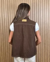 Chaleco de denim color marrón, de corte holgado, con cuello camisero, cierre frontal de botones metálicos y bolsillos appliqués con solapa en el pecho.